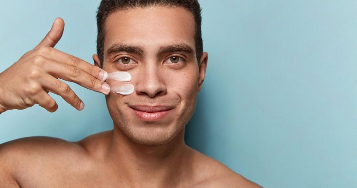 Young man applying moisturiser under his eye, part of a men's skincare routine in Dubai